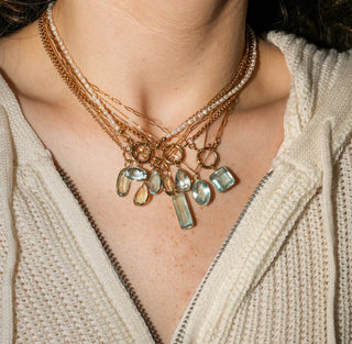 Necklace with multicolored gemstones worn by a person in a beige sweater.