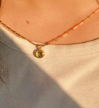 Gold necklace with a green gemstone pendant worn by a person in a white shirt.